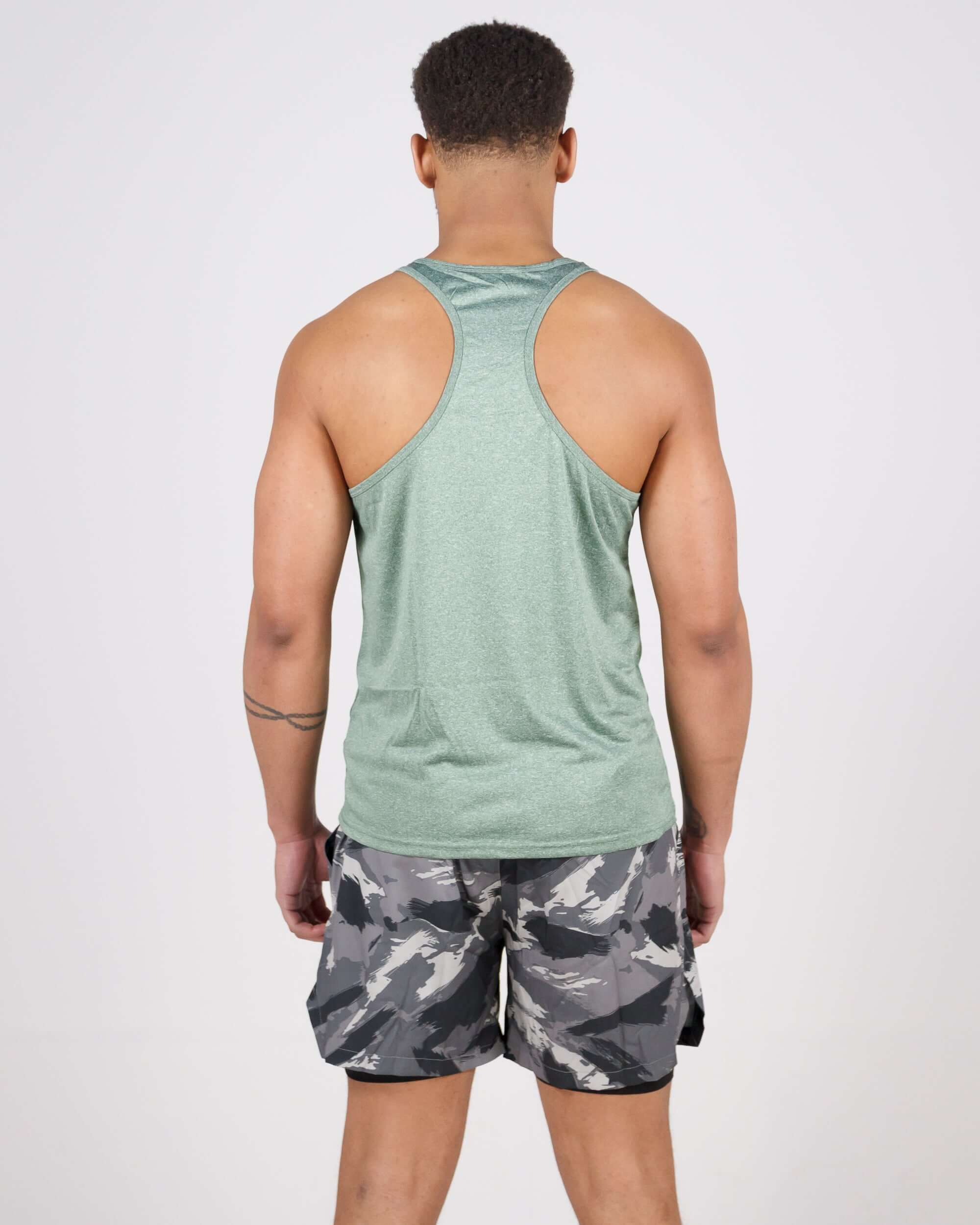 Man wearing light green Pinnacle Slim Fit Tank Top and camouflage shorts, facing backward, showcasing the tank top's slim fit and comfort.