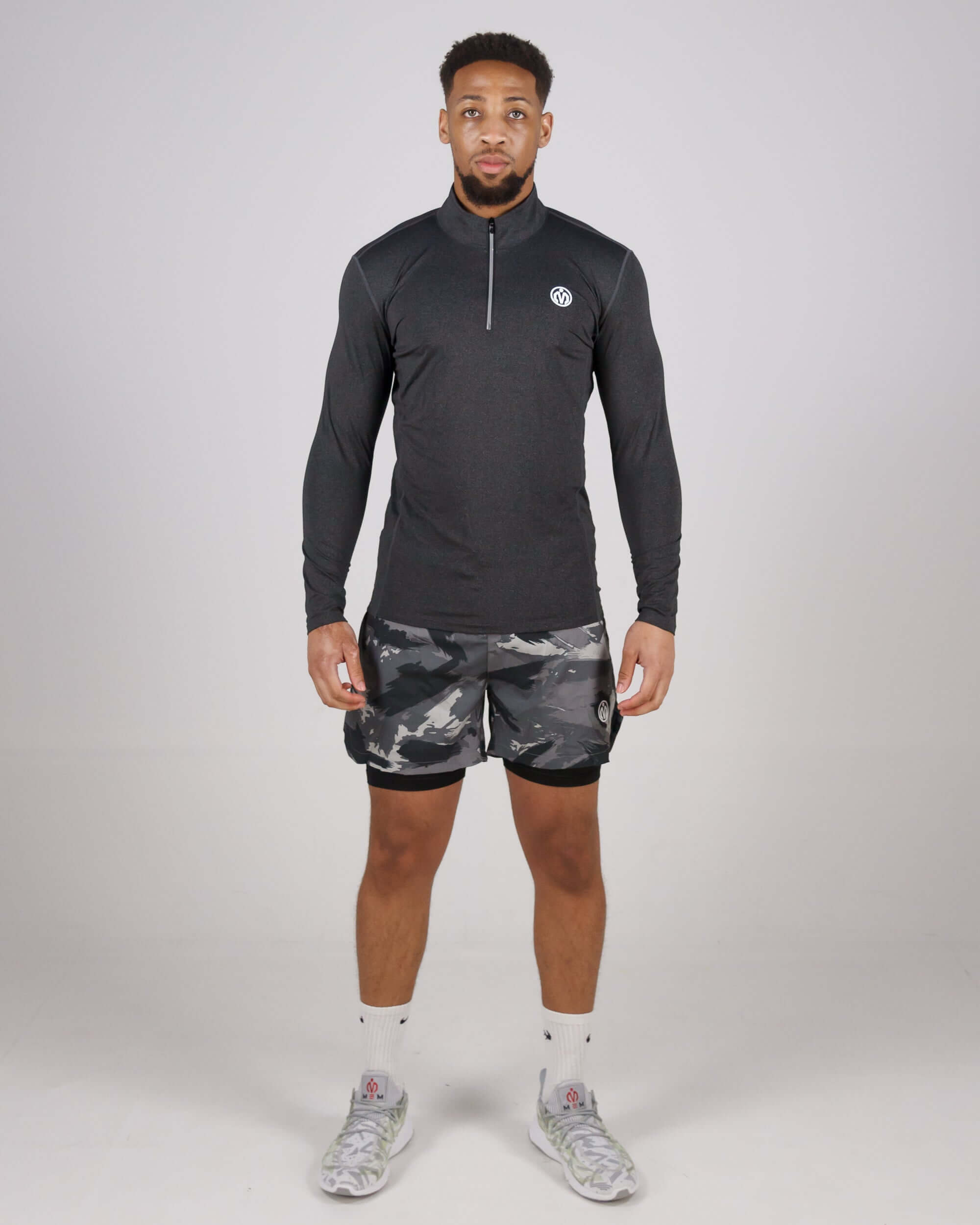 Man wearing Pinnacle Dry-Fit Long Sleeve Half Zip Training Top in grey, paired with camouflage shorts and white sneakers.