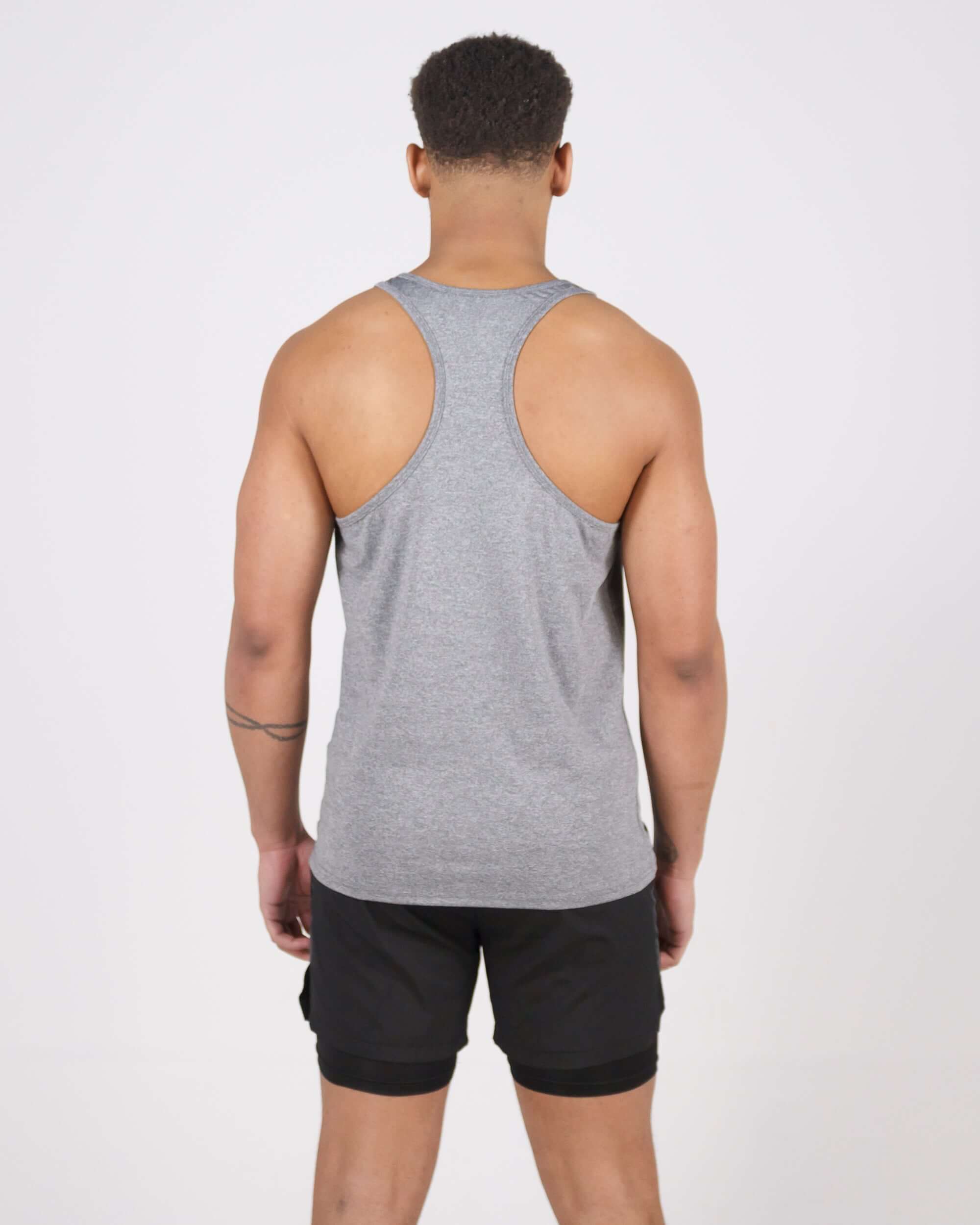 Man wearing grey Pinnacle Slim Fit Tank Top with black shorts, showing the back view of the tank top's design and fit.